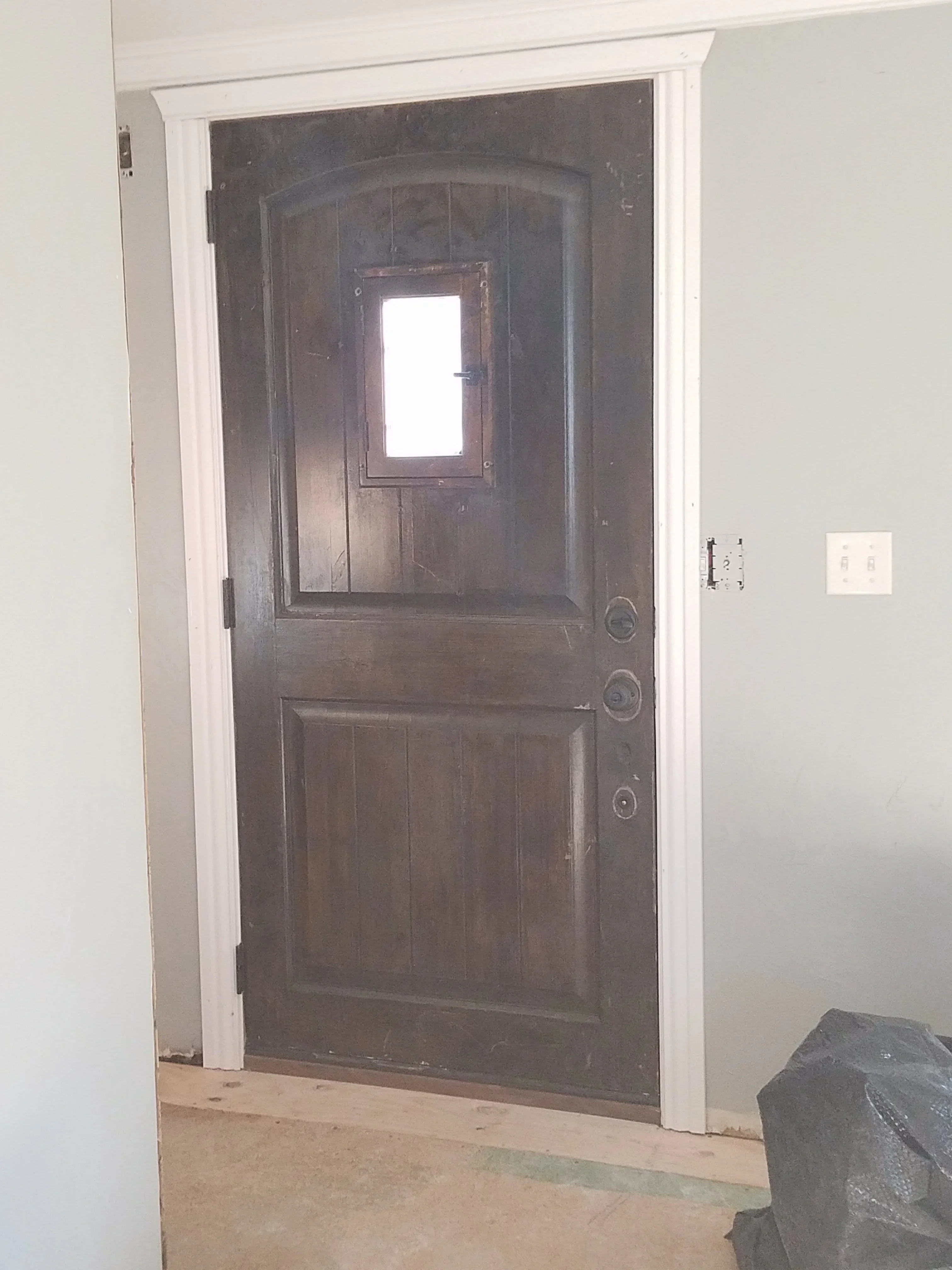 Dark wood six-panel entry door with arched top and glass window, white trim frame