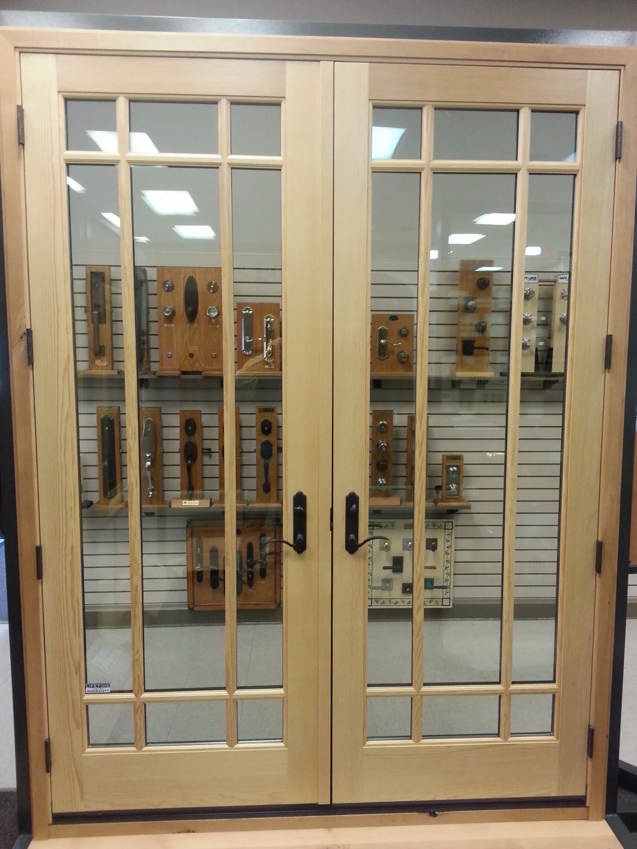 Wooden double doors with glass panes displaying door hardware samples and fixtures