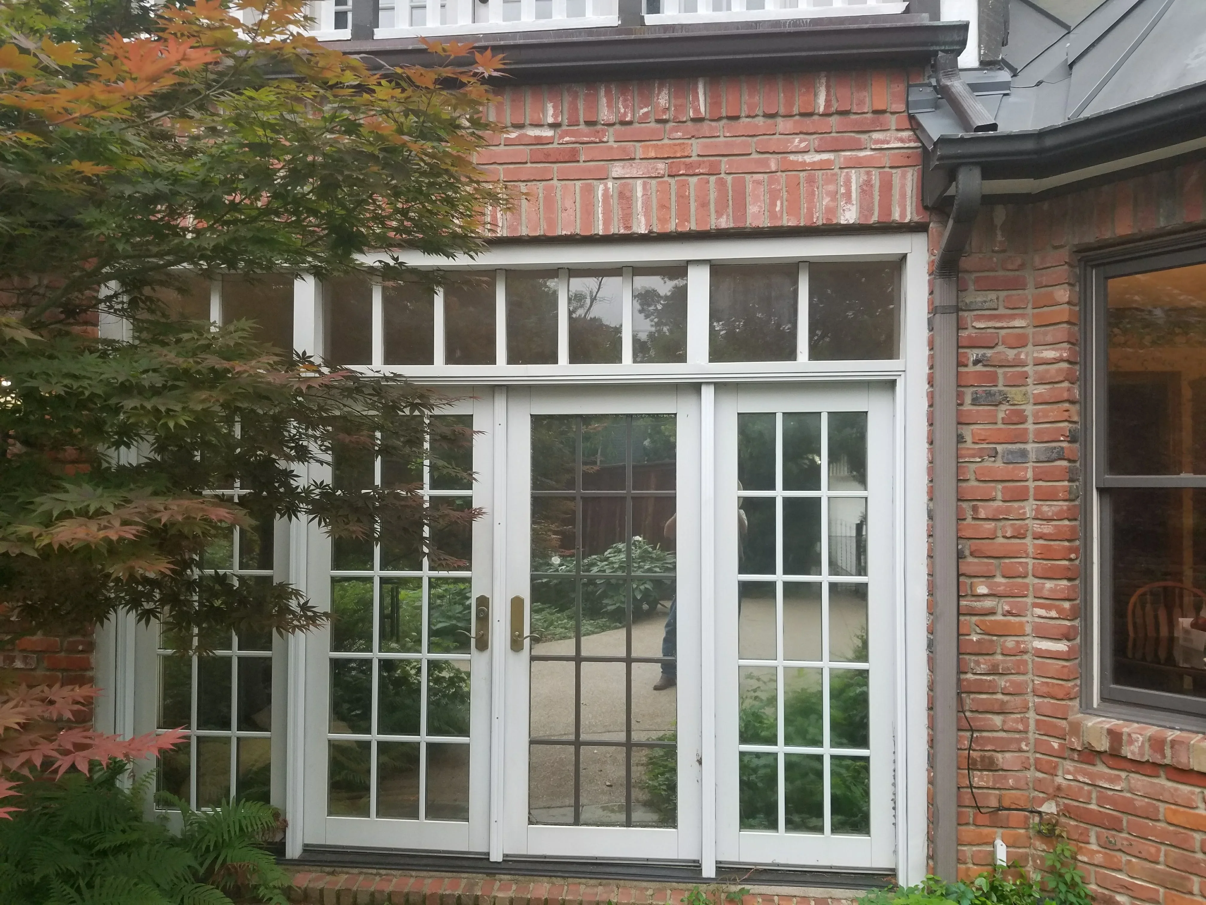 White French doors with grid glass panes installed on red brick home exterior with transom windows