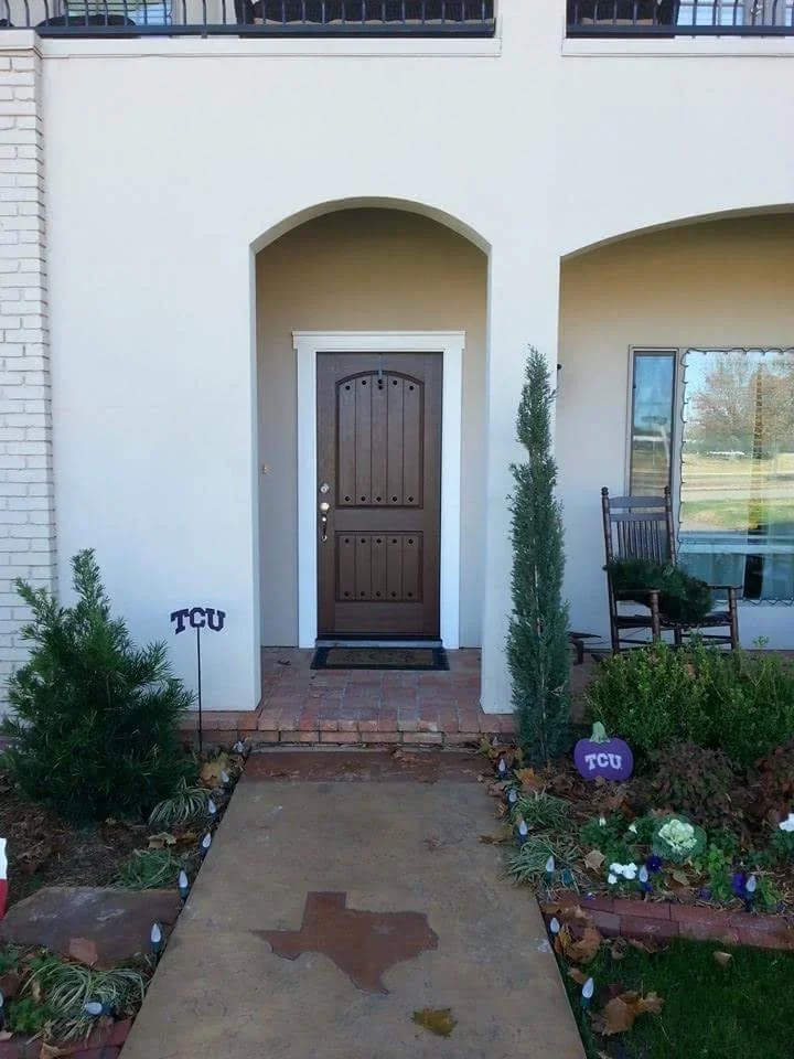 Dark wood arched entry door with white trim in stucco archway