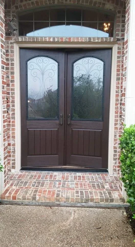Double brown entry doors with ornamental iron glass panels and arched transom window in brick exterior