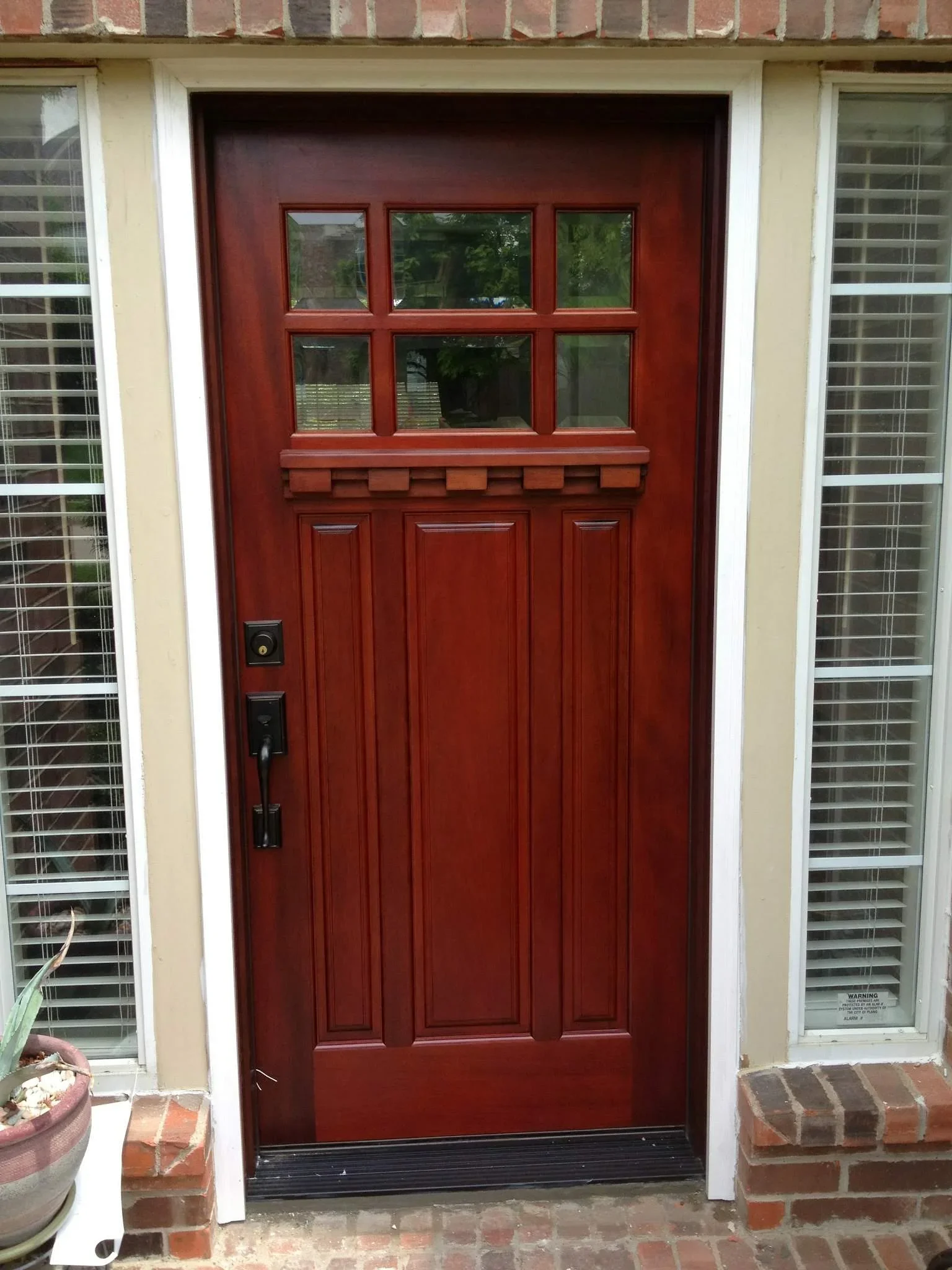 Red six-panel entry door with six-light windows, black hardware, and brick molding installation