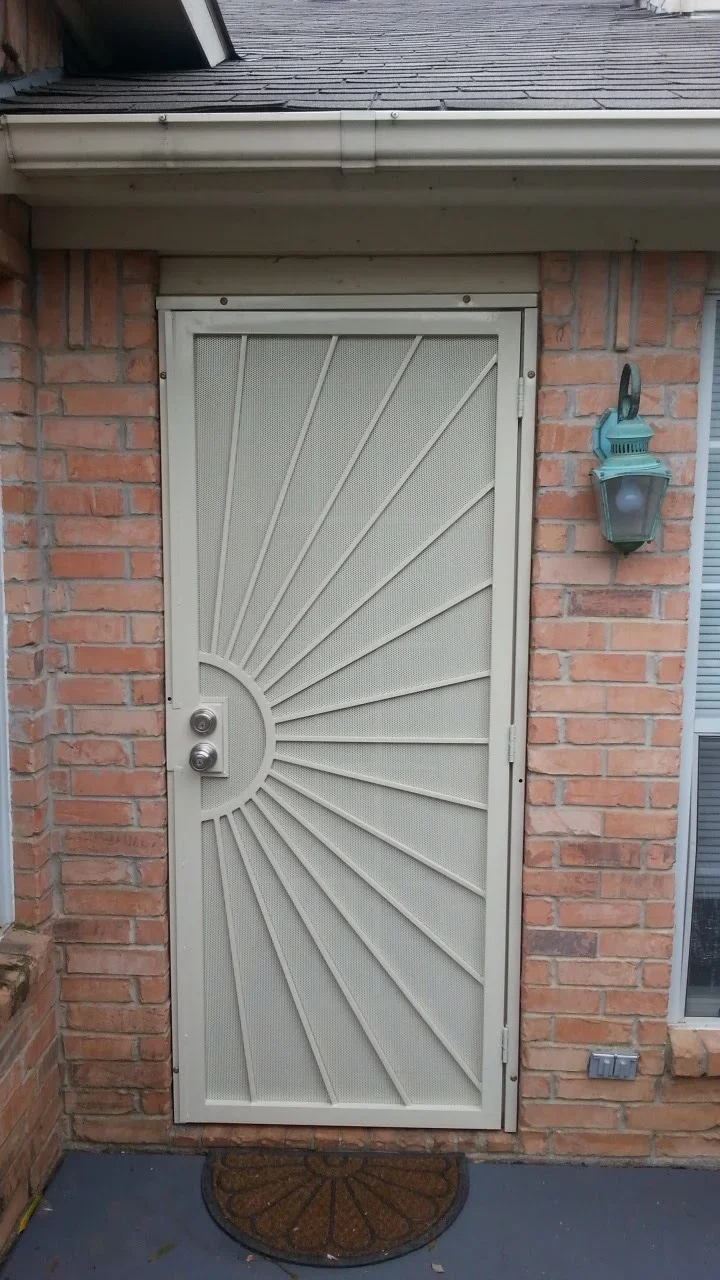 White aluminum security door with sunburst design and mesh screen on brick home exterior