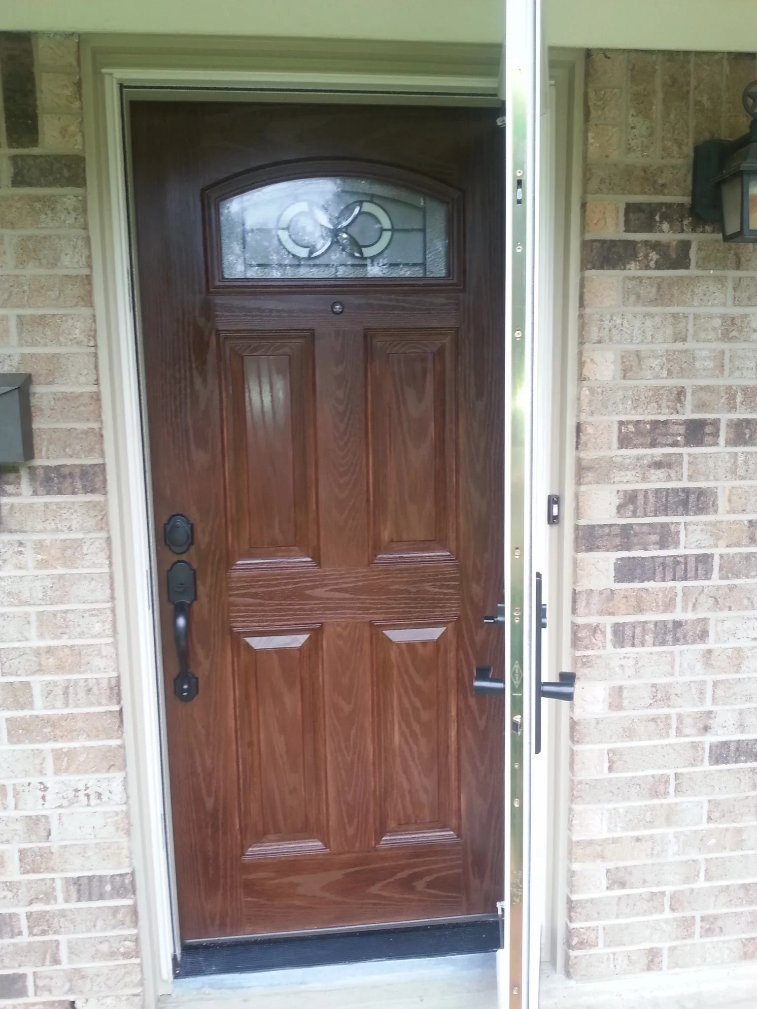 Six-panel wood grain entry door with arched transom window and black hardware on brick facade