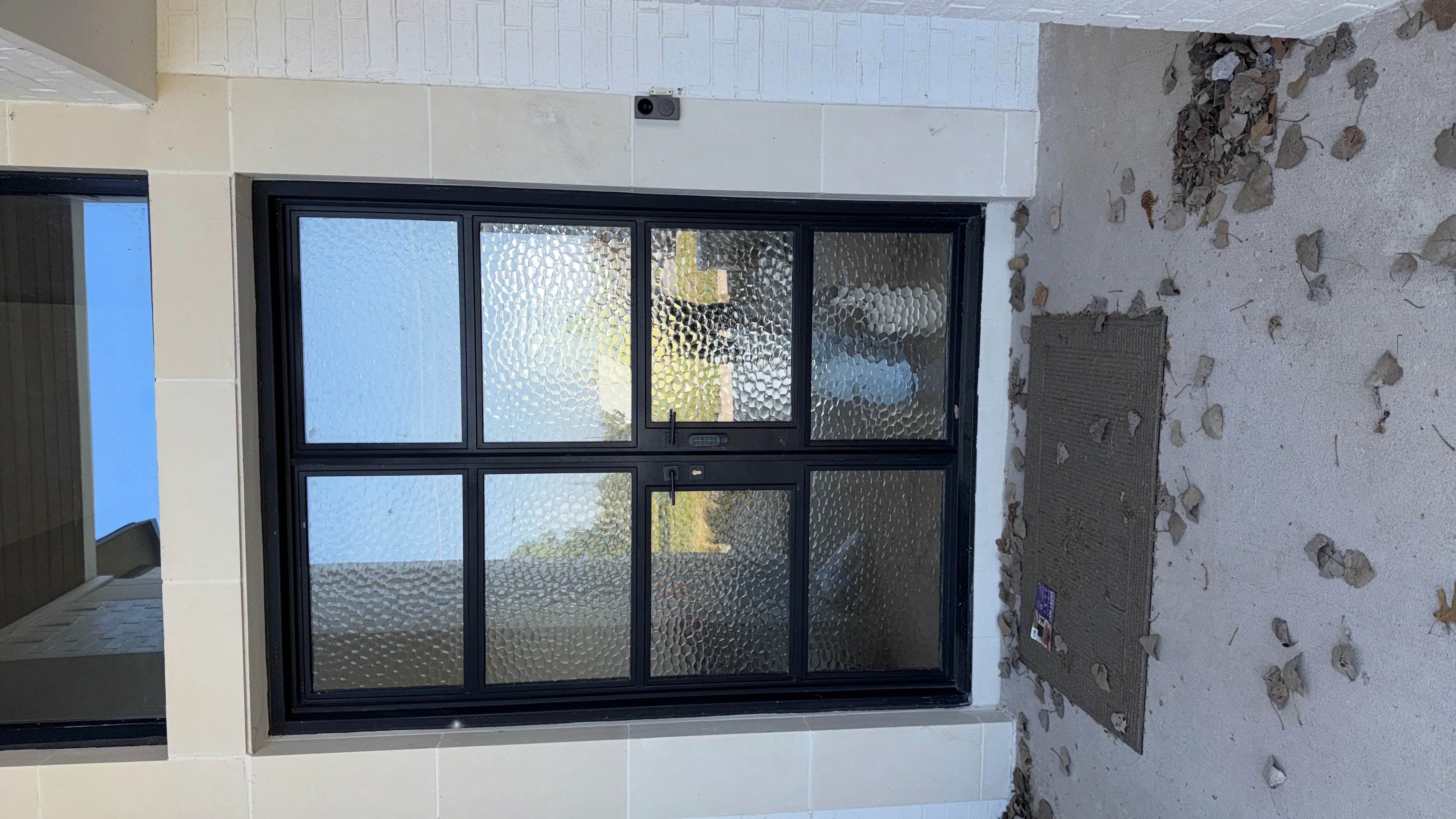 Black aluminum frame door with eight textured glass panels installed in white tile wall