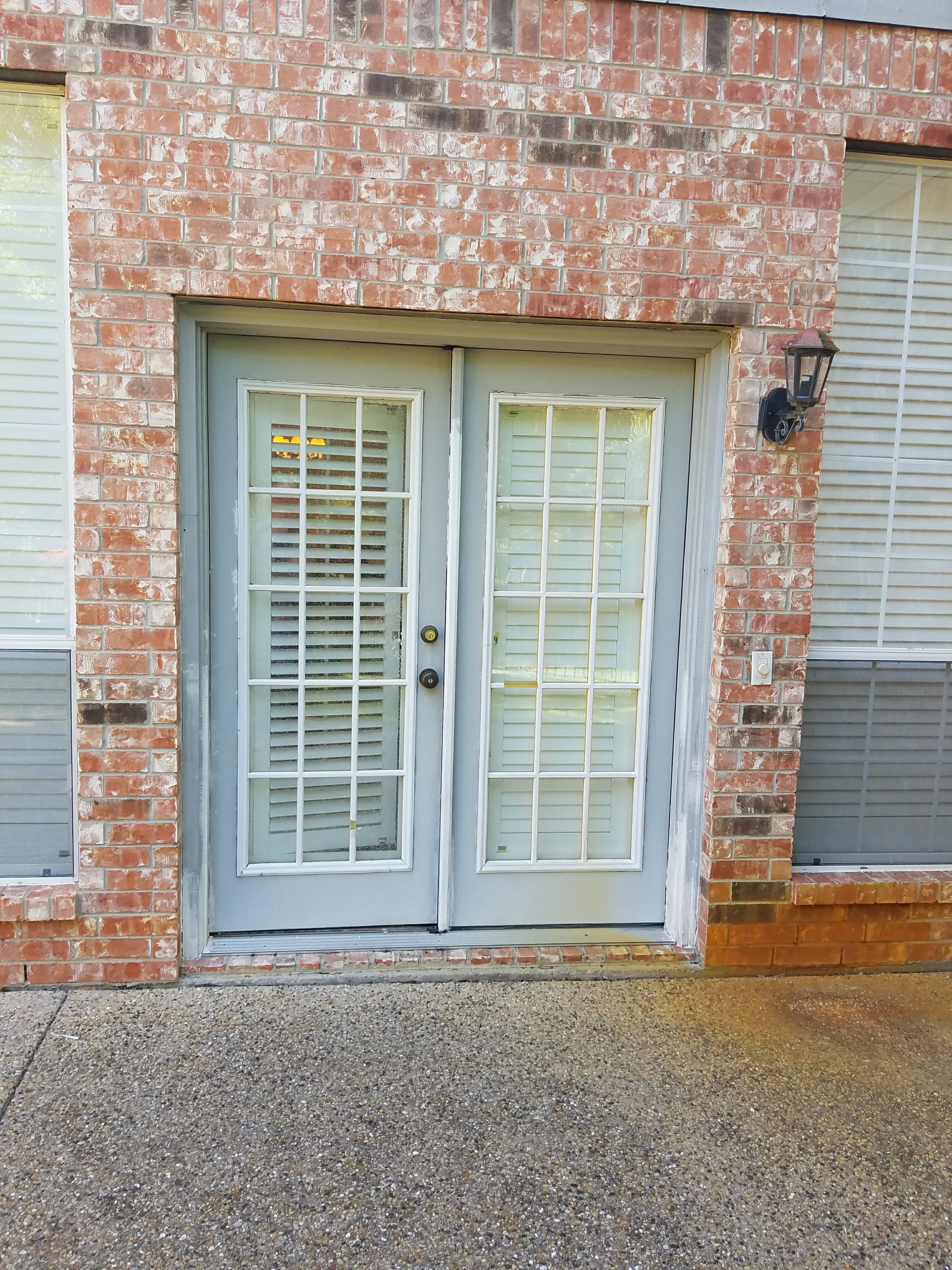Cream-framed French doors with 15-lite windows and plantation shutters installed in red brick exterior