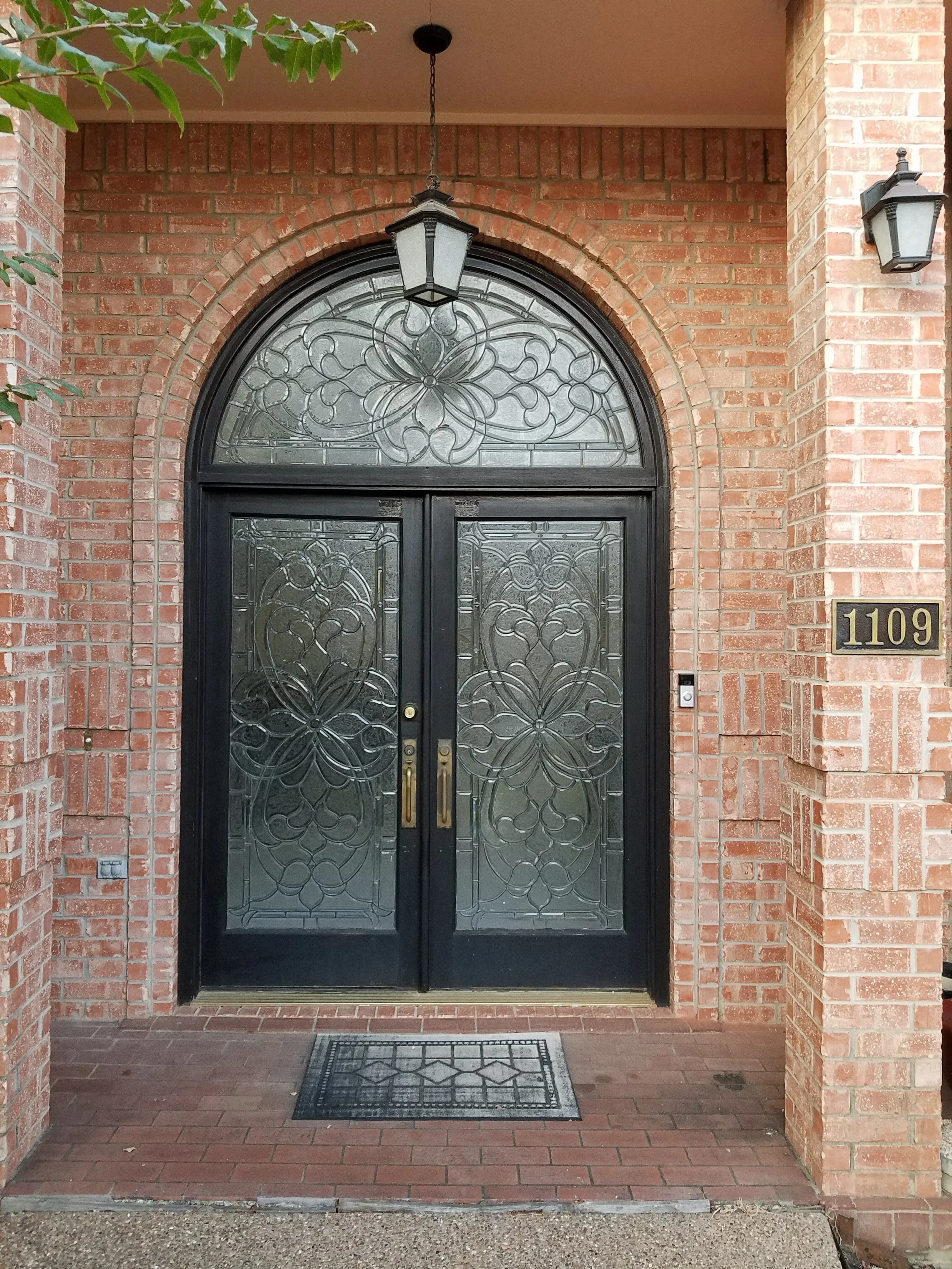 Black arched double entry door with decorative beveled glass and floral patterns in brick entryway