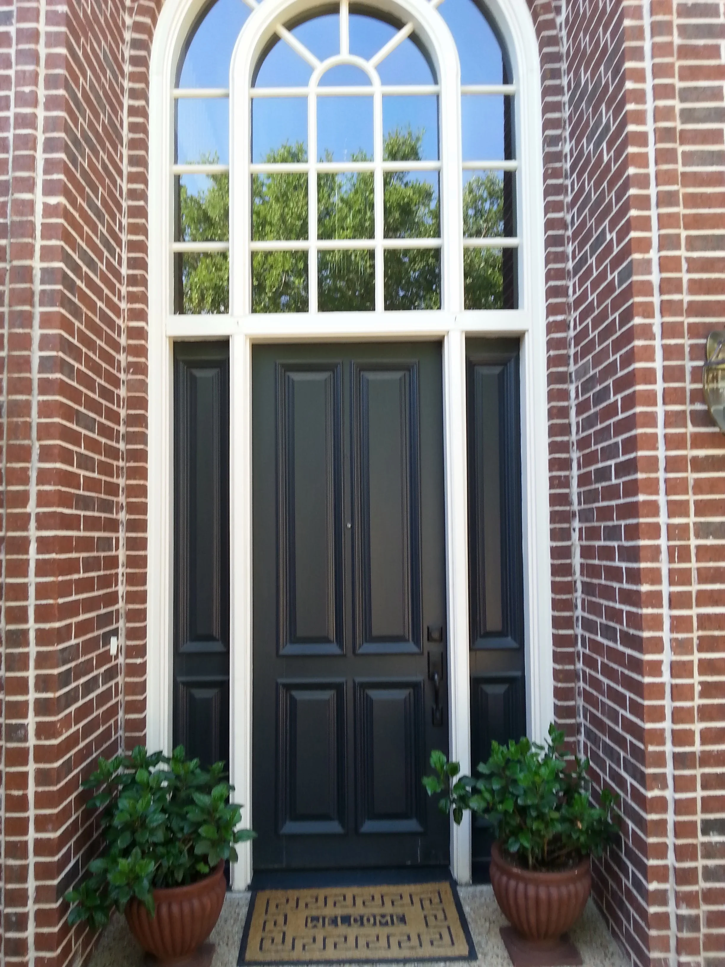 Black six-panel entry door with white-framed arched transom window and sidelights in brick exterior