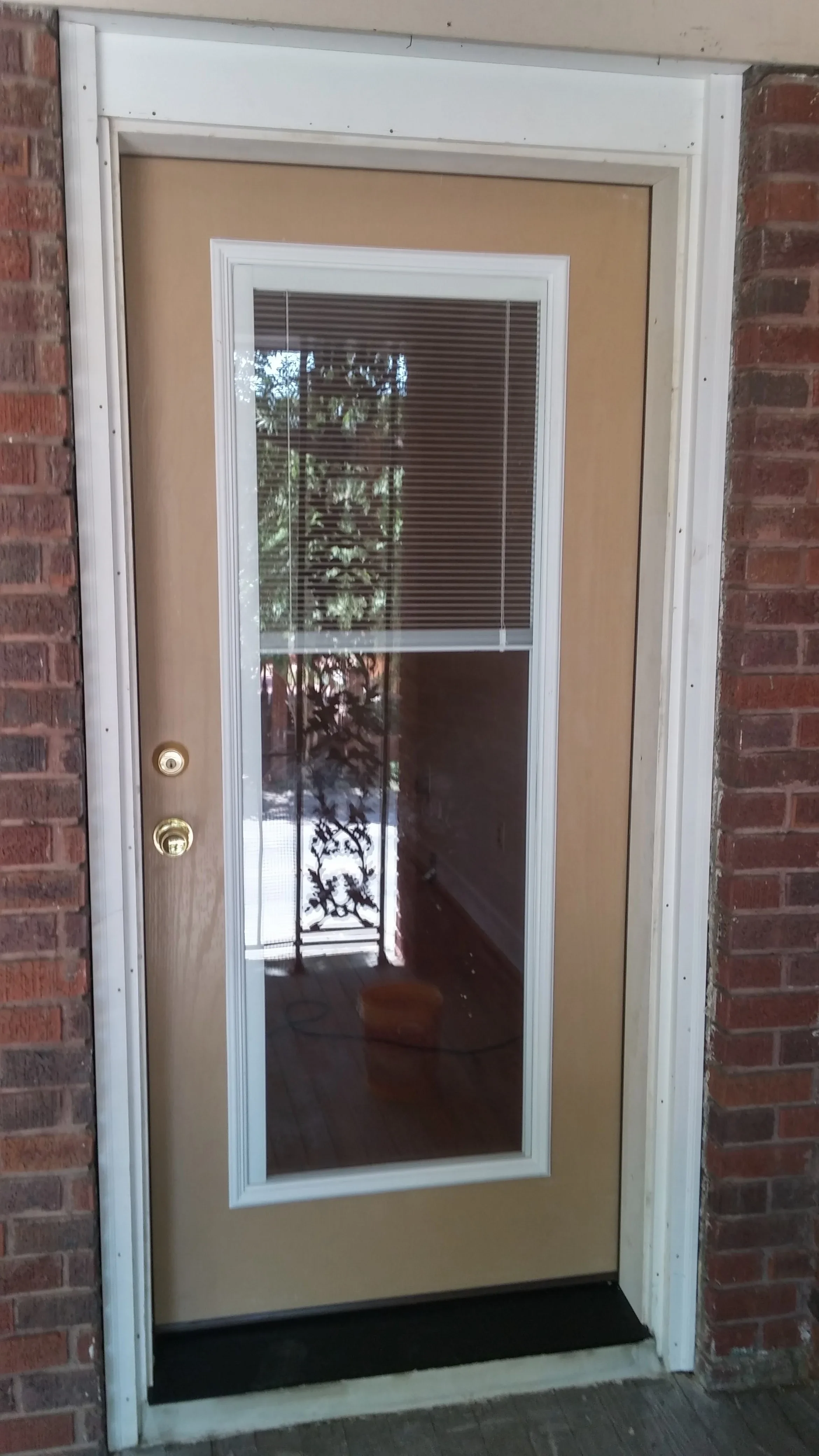 White-framed glass entry door with integrated mini blinds and brass hardware on brick exterior