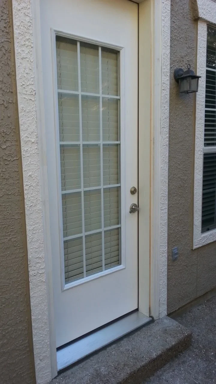 White-framed full-glass entry door with 15-pane grid pattern and brass hardware