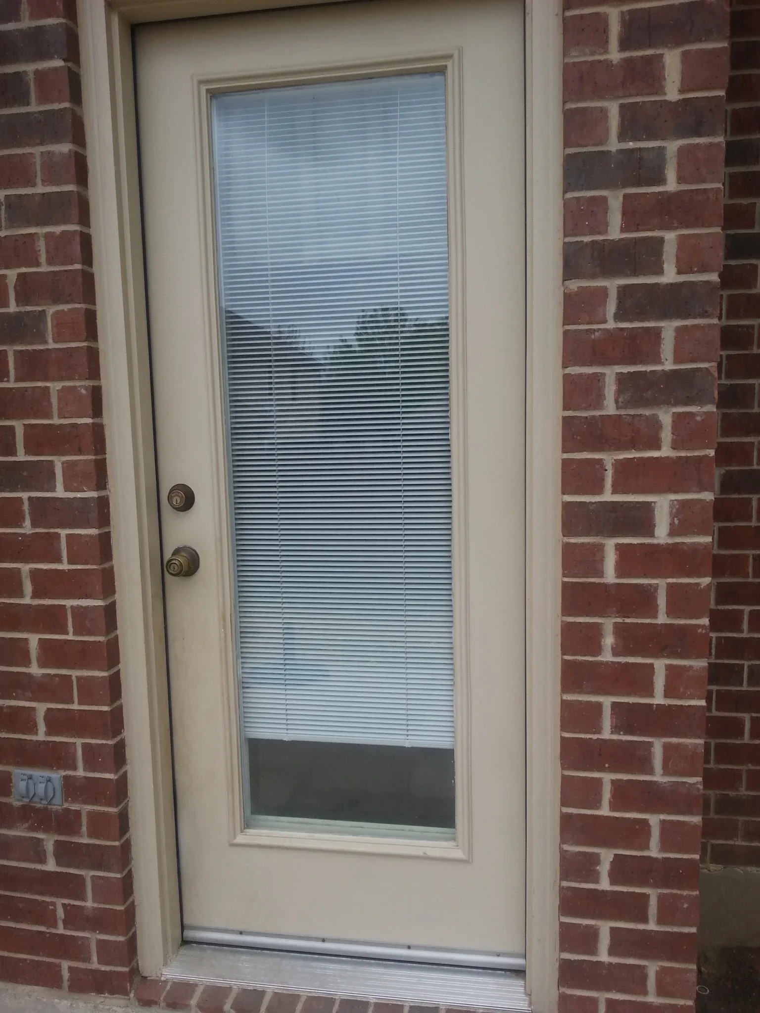 Cream-framed exterior door with integrated blinds and dual-pane glass, installed between red brick