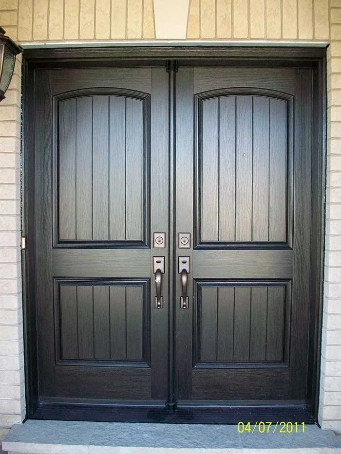 Dark wood-grain fiberglass double doors with arched panels and vertical grooves installed in entryway