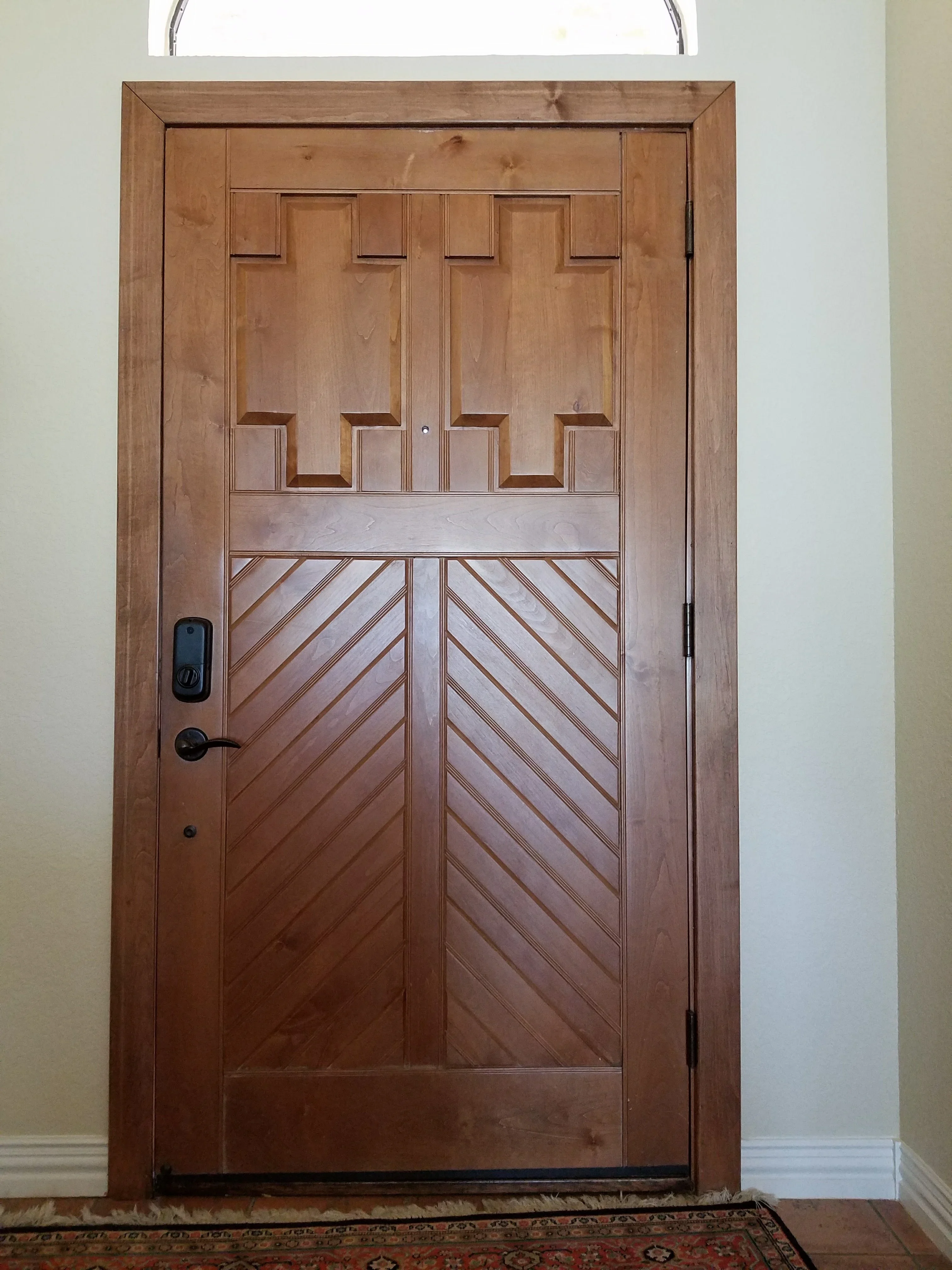 Solid wood entry door with geometric panels, diagonal V-groove lower section, and electronic lock hardware