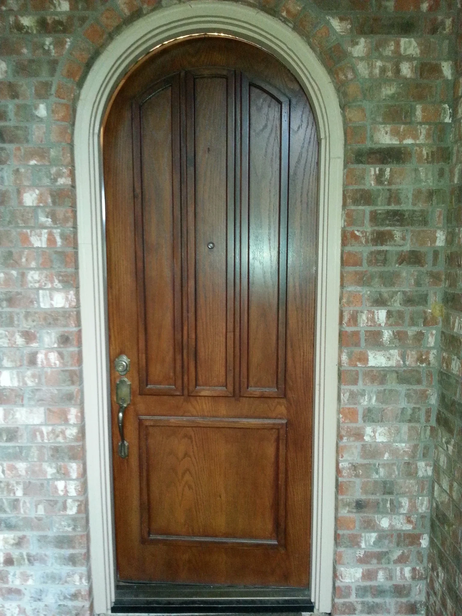 Arched wooden entry door with five panels and cream molding on brick wall