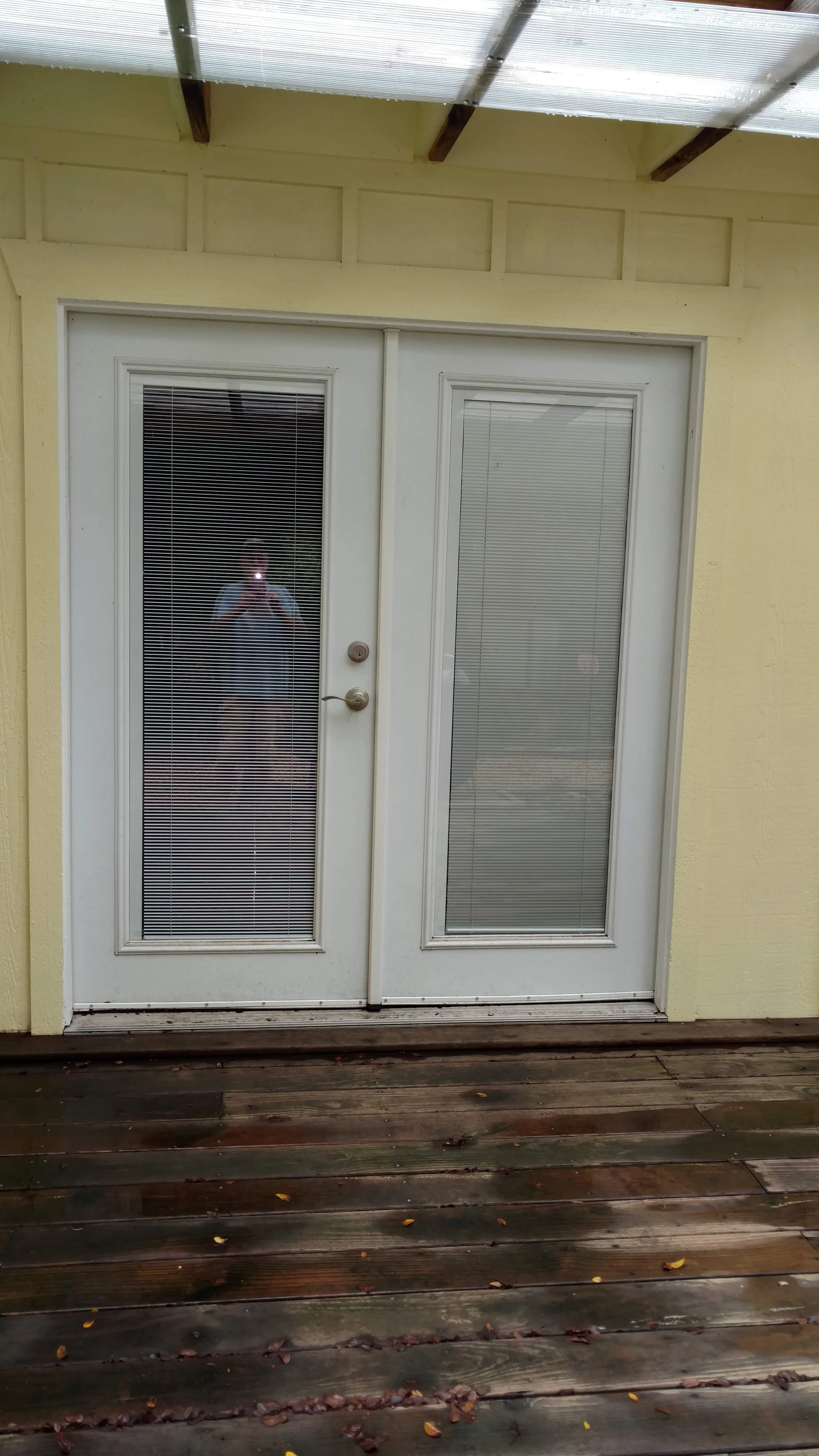 White French patio doors with built-in mini blinds, installed in yellow wall with wood deck
