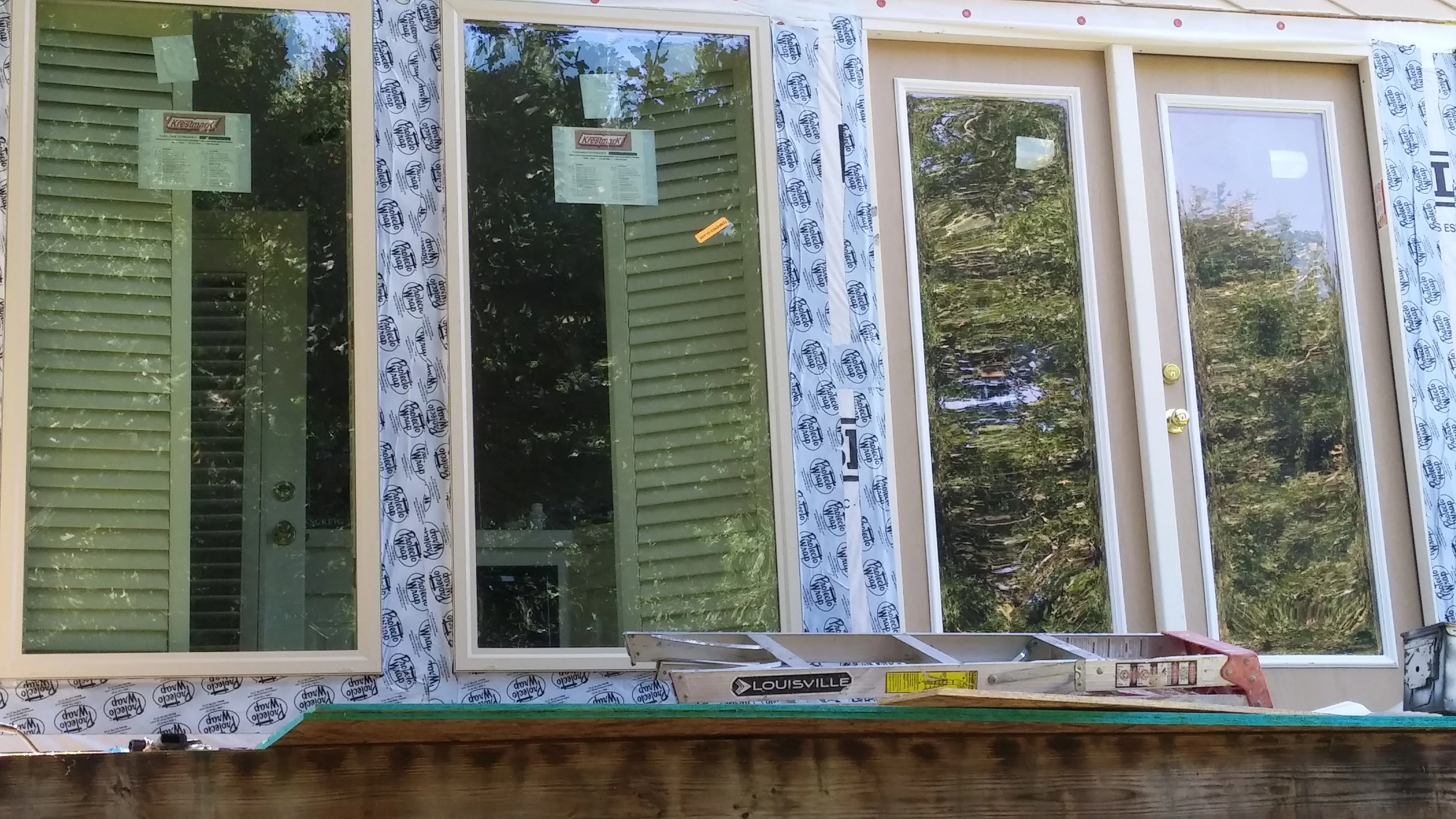 White-framed patio doors and louvered door installation with house wrap and weatherproofing