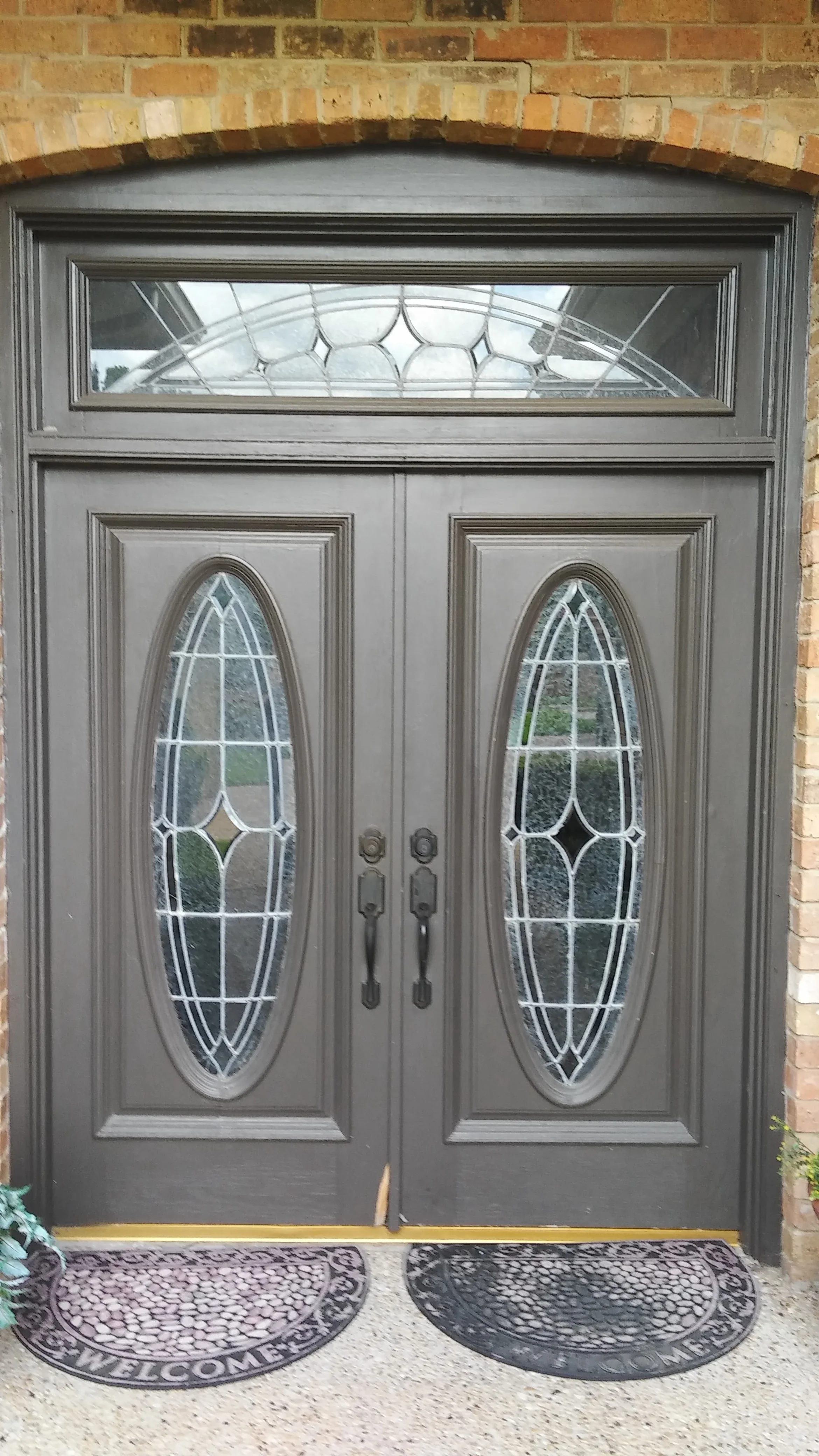 Gray double entry doors with oval glass panels and geometric muntins, transom window above
