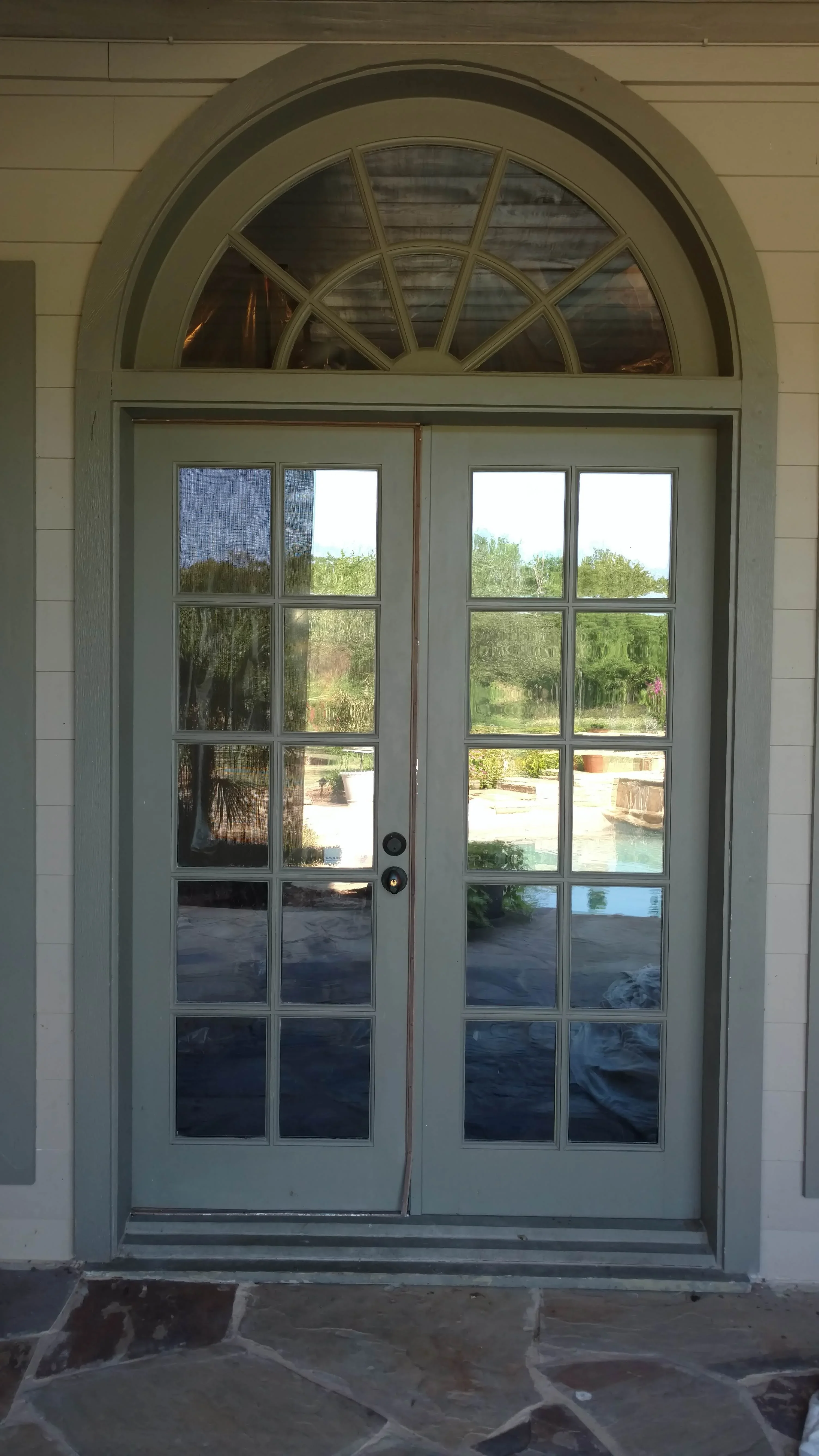 Sage-framed French doors with arched transom, ten-pane glass panels, landscape view