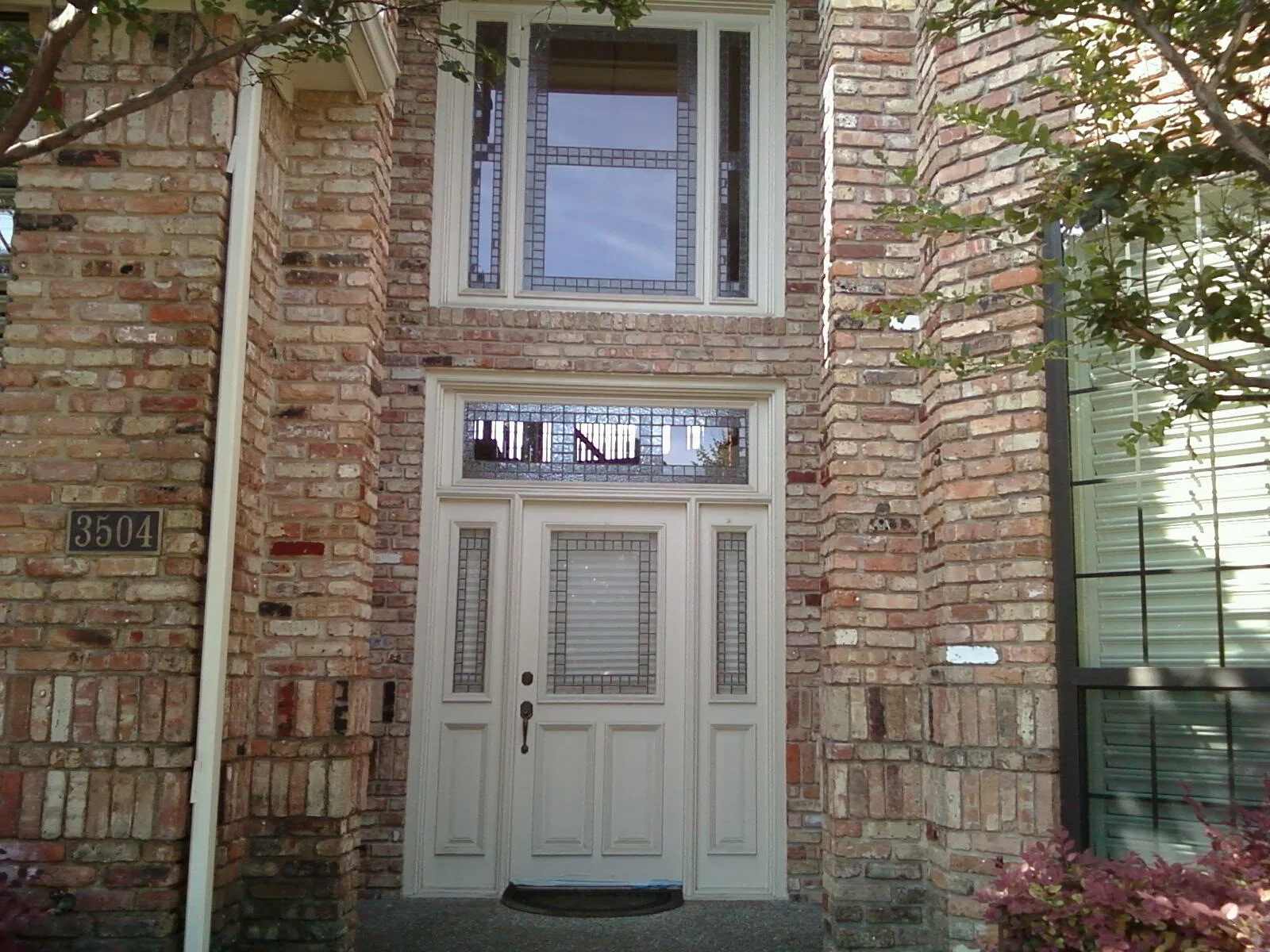 White entry door with sidelights and transom windows on red brick facade