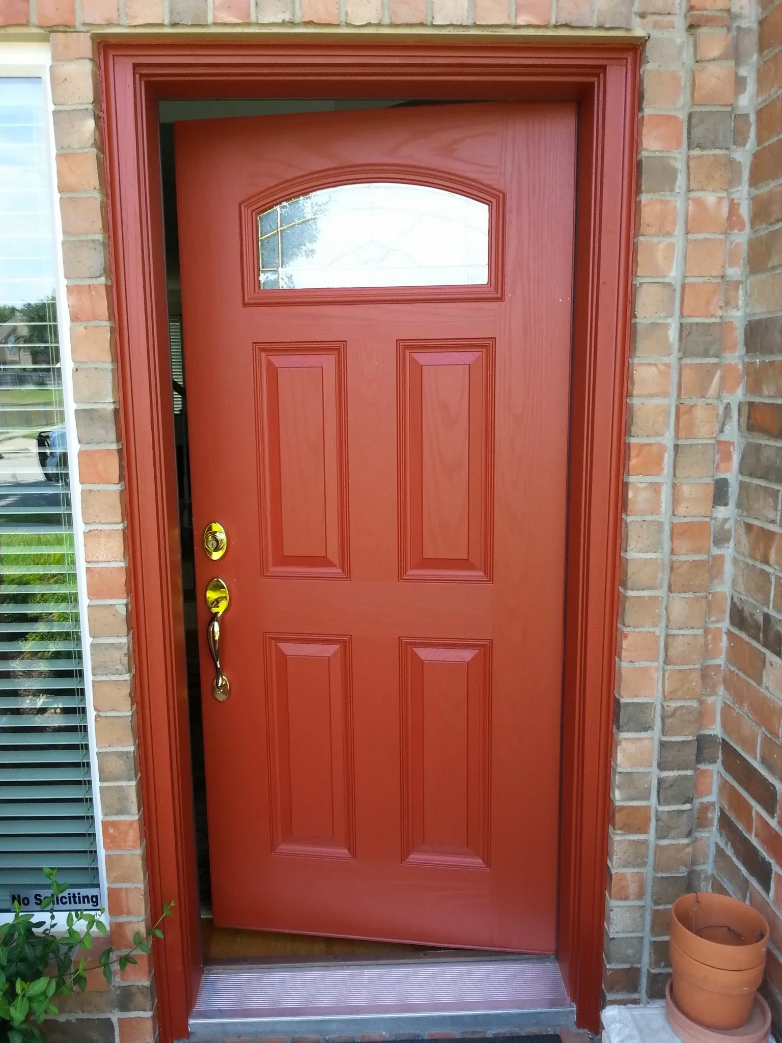 Red six-panel entry door with transom window and brass hardware on brick facade