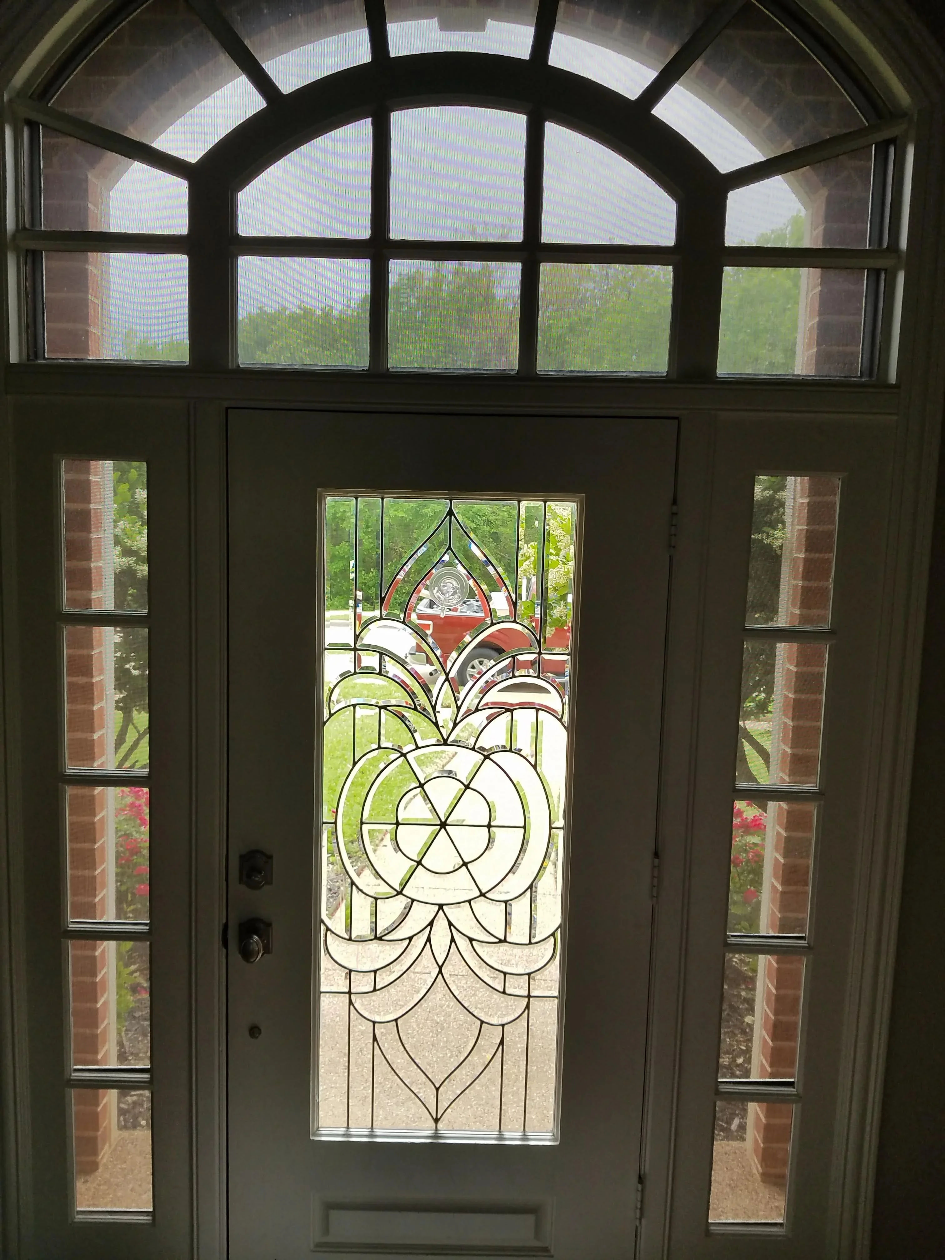Stained glass entry door with geometric floral pattern, sidelights, and transom window