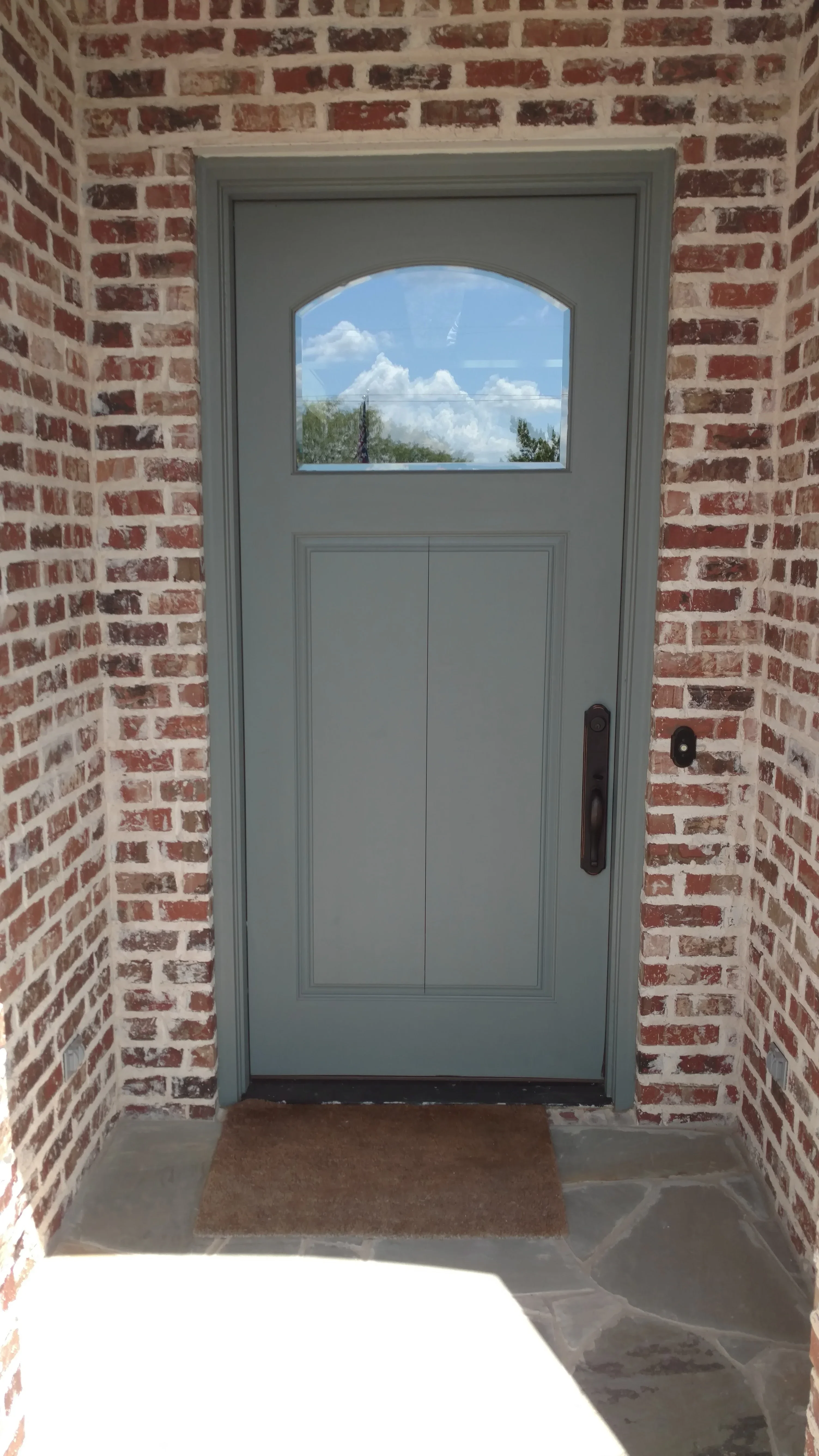 Gray entry door with arched window in brick entryway, dark hardware