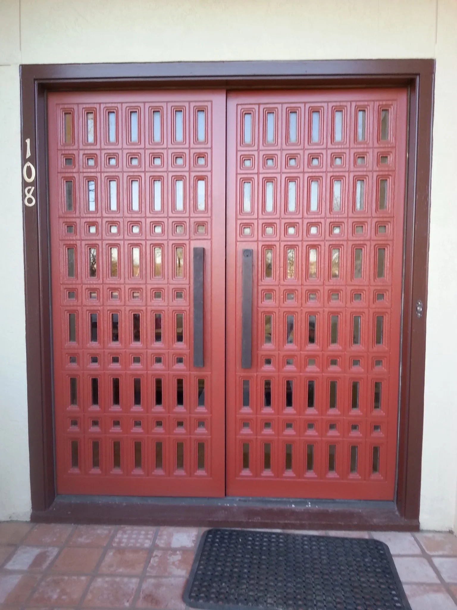 Red double entry doors with geometric glass panel grid pattern and bronze frame