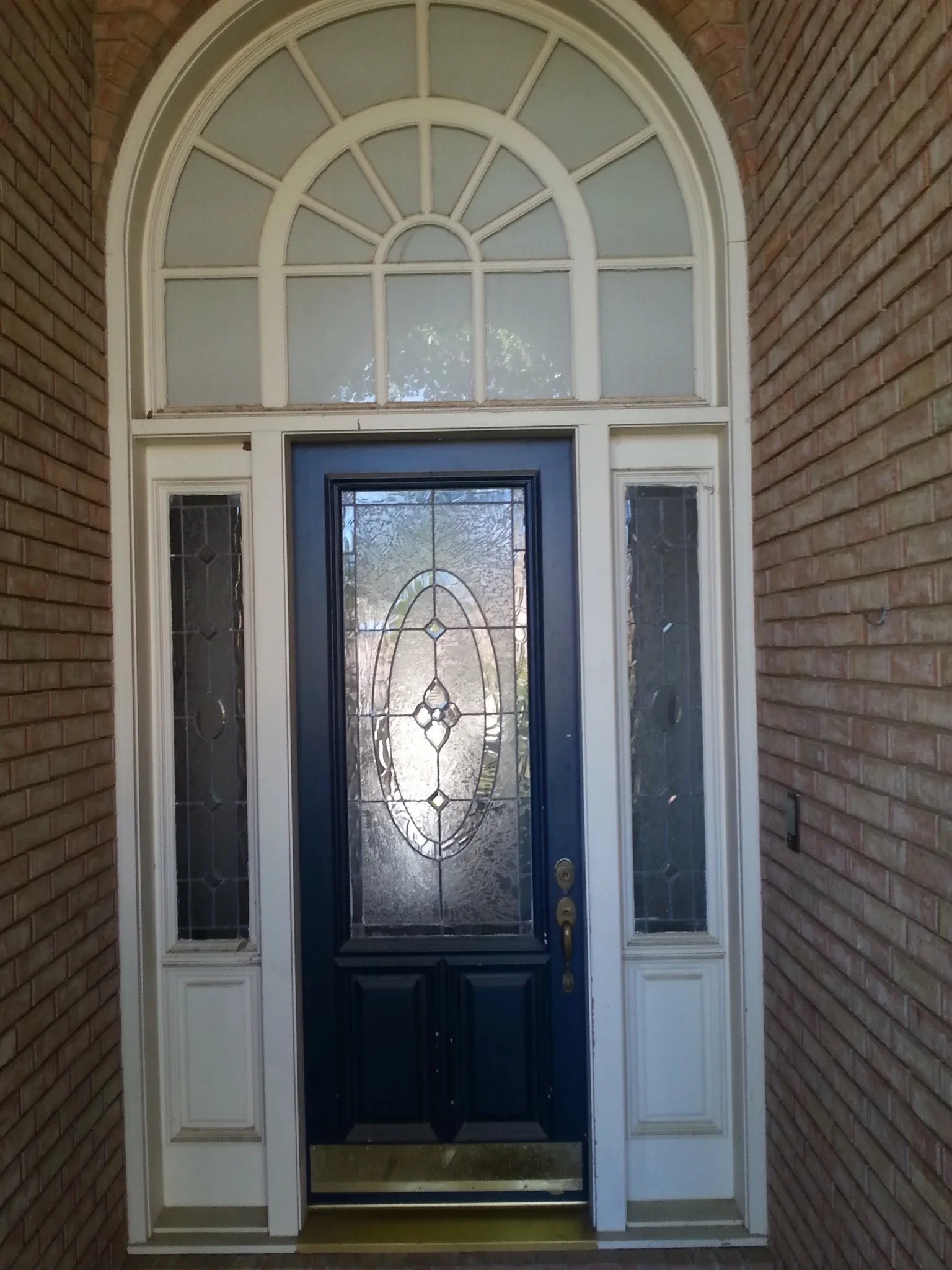 Black entry door with leaded glass insert, cream sidelights, and arched transom window on brick home