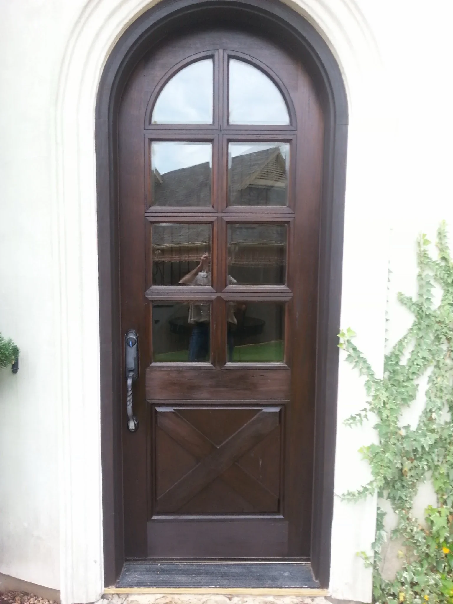 Dark wood arched entry door with ten-pane windows and X-pattern panel in white stucco archway